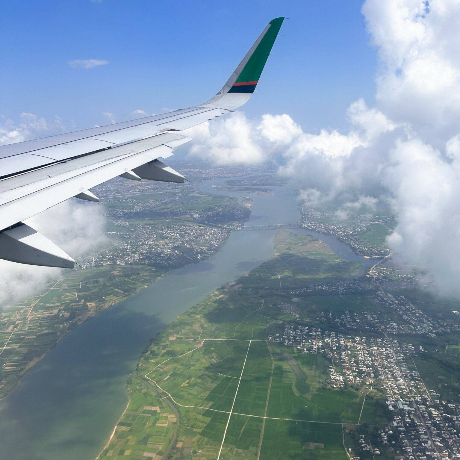 Blick aus einem Flugzeug auf die Tragfläche und eine Landschaft mit einem Fluss.