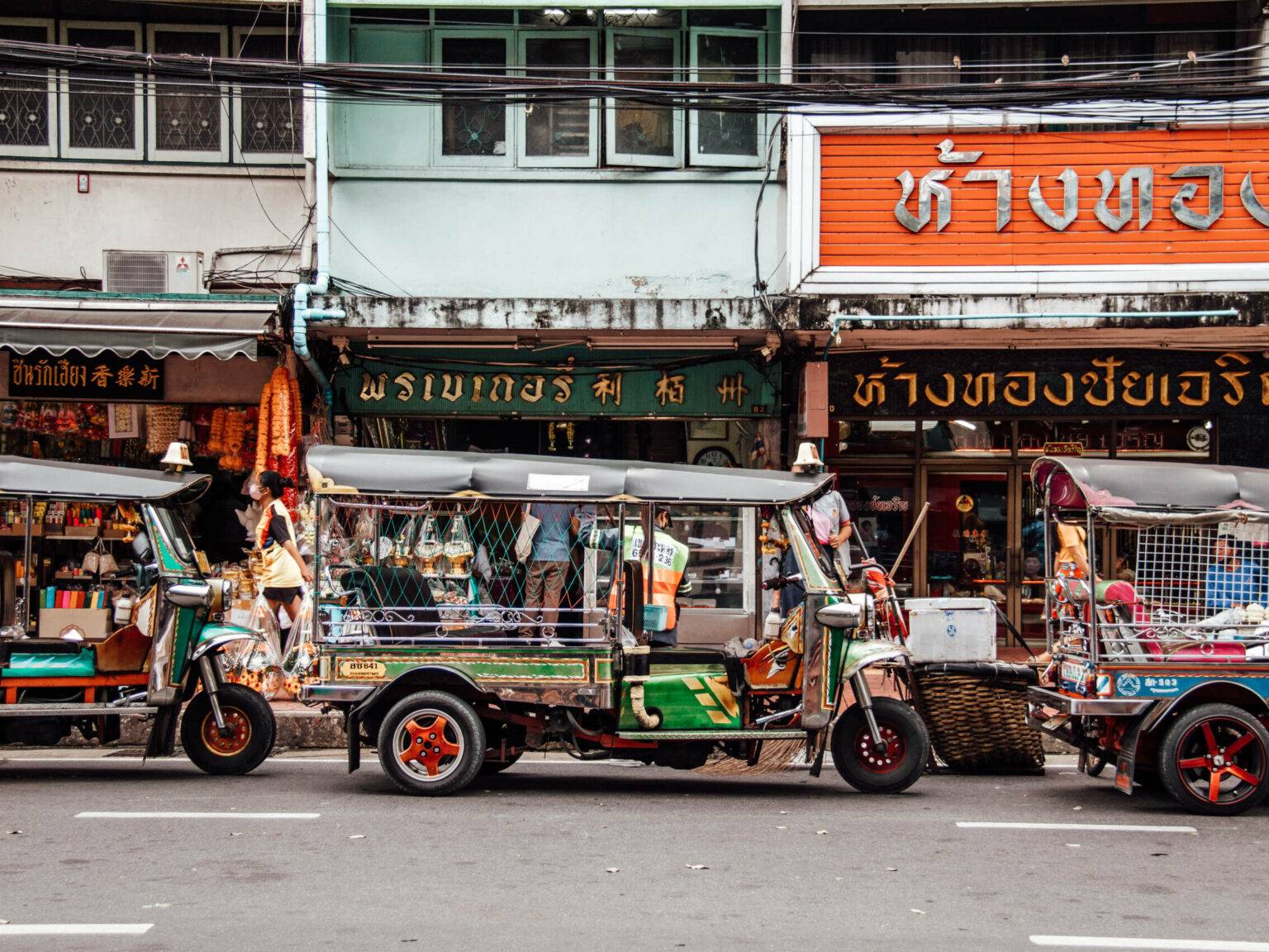 Ein vollbeladenes Tuk Tuk in einer typischen Straße in Bangkok.