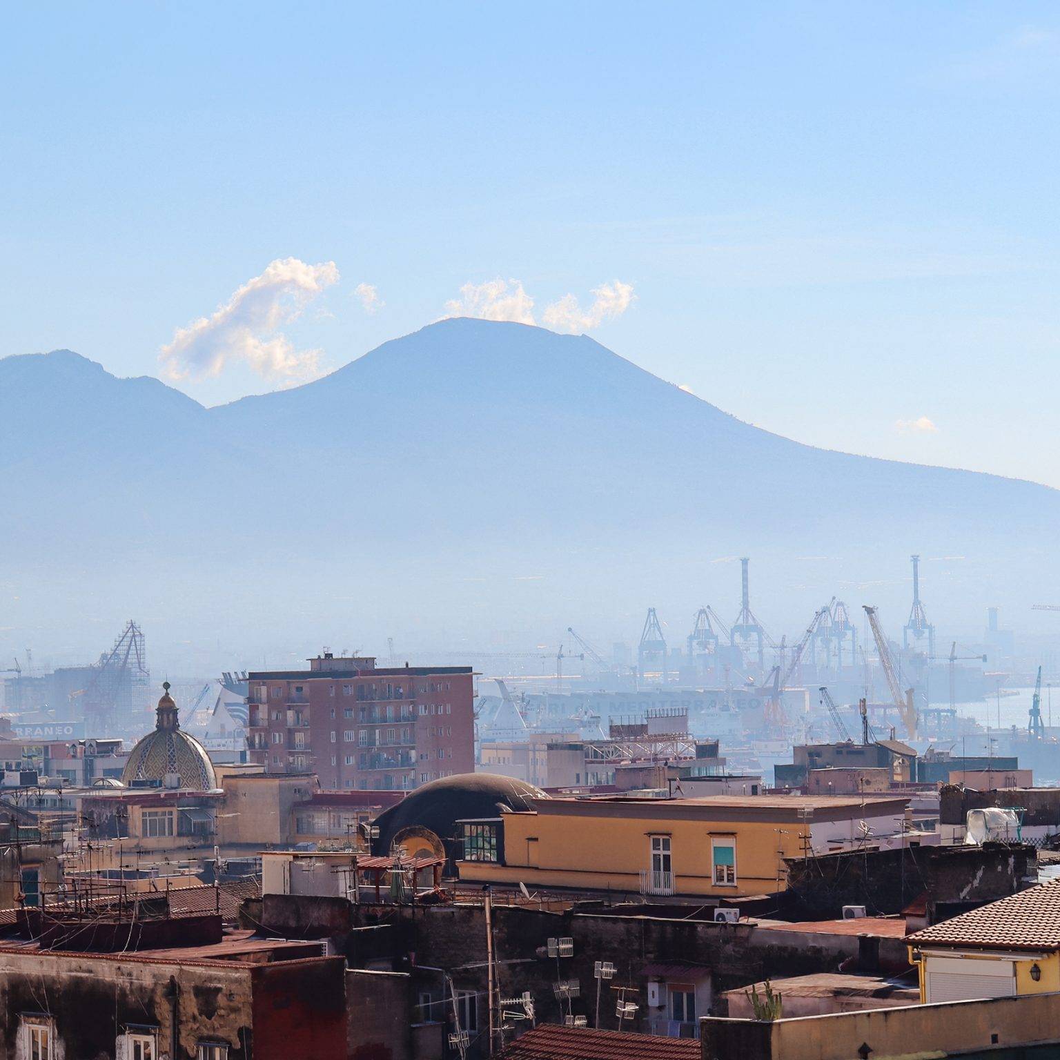 Der Vulkan Vesuv liegt hinter der sandfarbenen Skyline Neapels im Nebel.