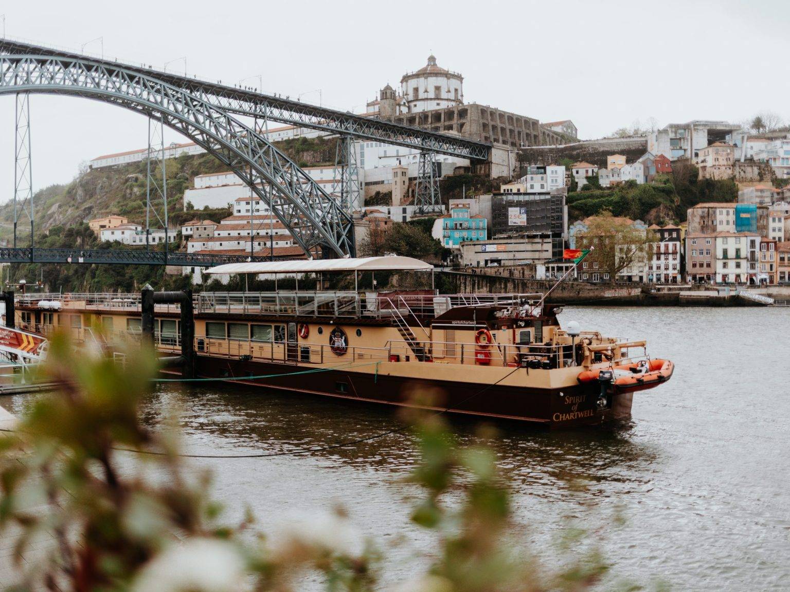 Ein dicht bebautes Ufer am Douro, links die imposante Metallbrücke und vorn ein Schiff, das vor Anker liegt.