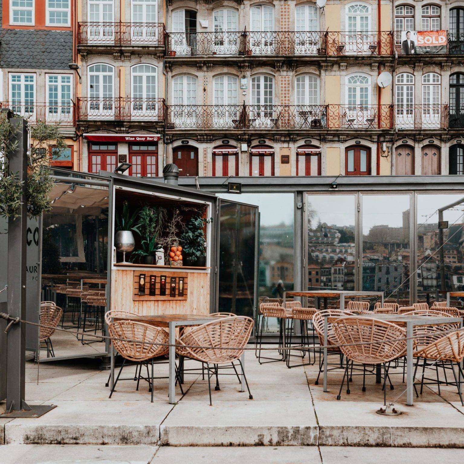 Kleines Café mit Rattanstühlen, im Hintergrund bunte Häuser mit kleinen Balkonen.