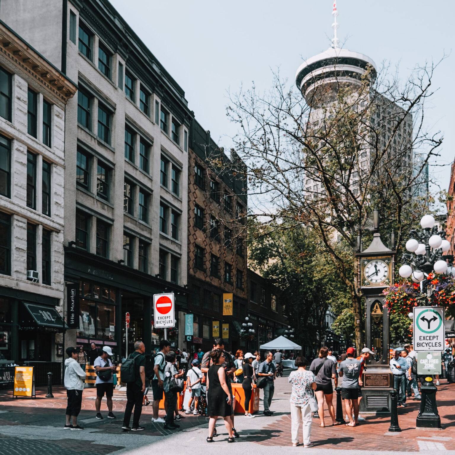 Die Water Street mit der Gastown Steam Clock und einigen Passanten, sowie der Space Needle im Hintergrund.