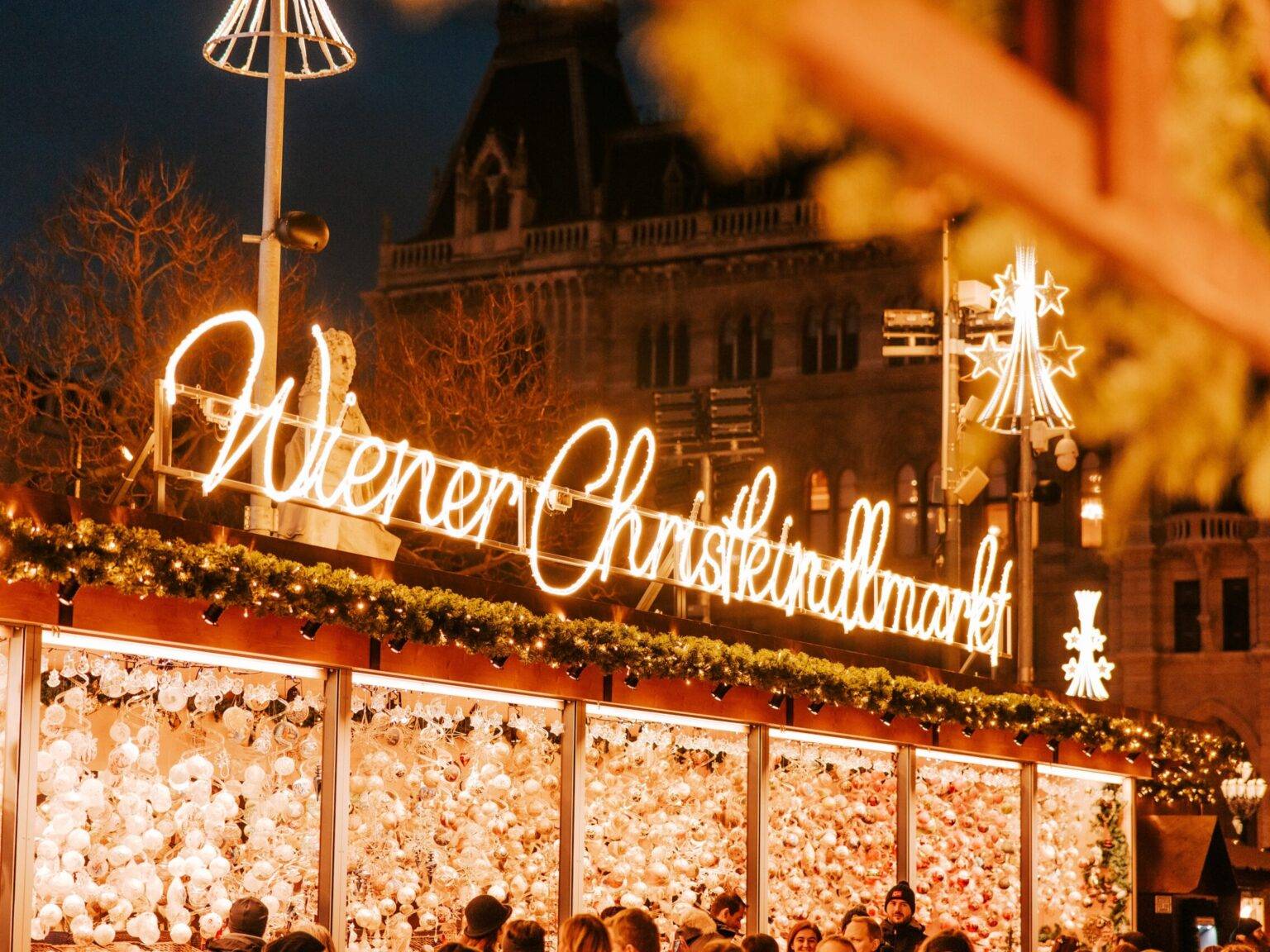 Ein Christbaumkugel-Stand mit dem leuchtenden Schriftzug "Wiener Christkindlmarkt" auf dem Dach.