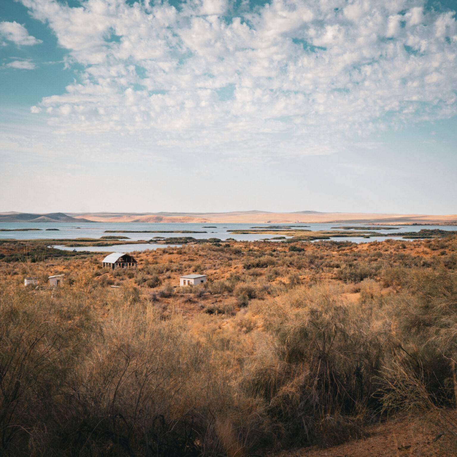 Blick auf den Aydarkul-See in Usbekistan, umgeben von trockener Wüstenlandschaft und vereinzelten Hütten