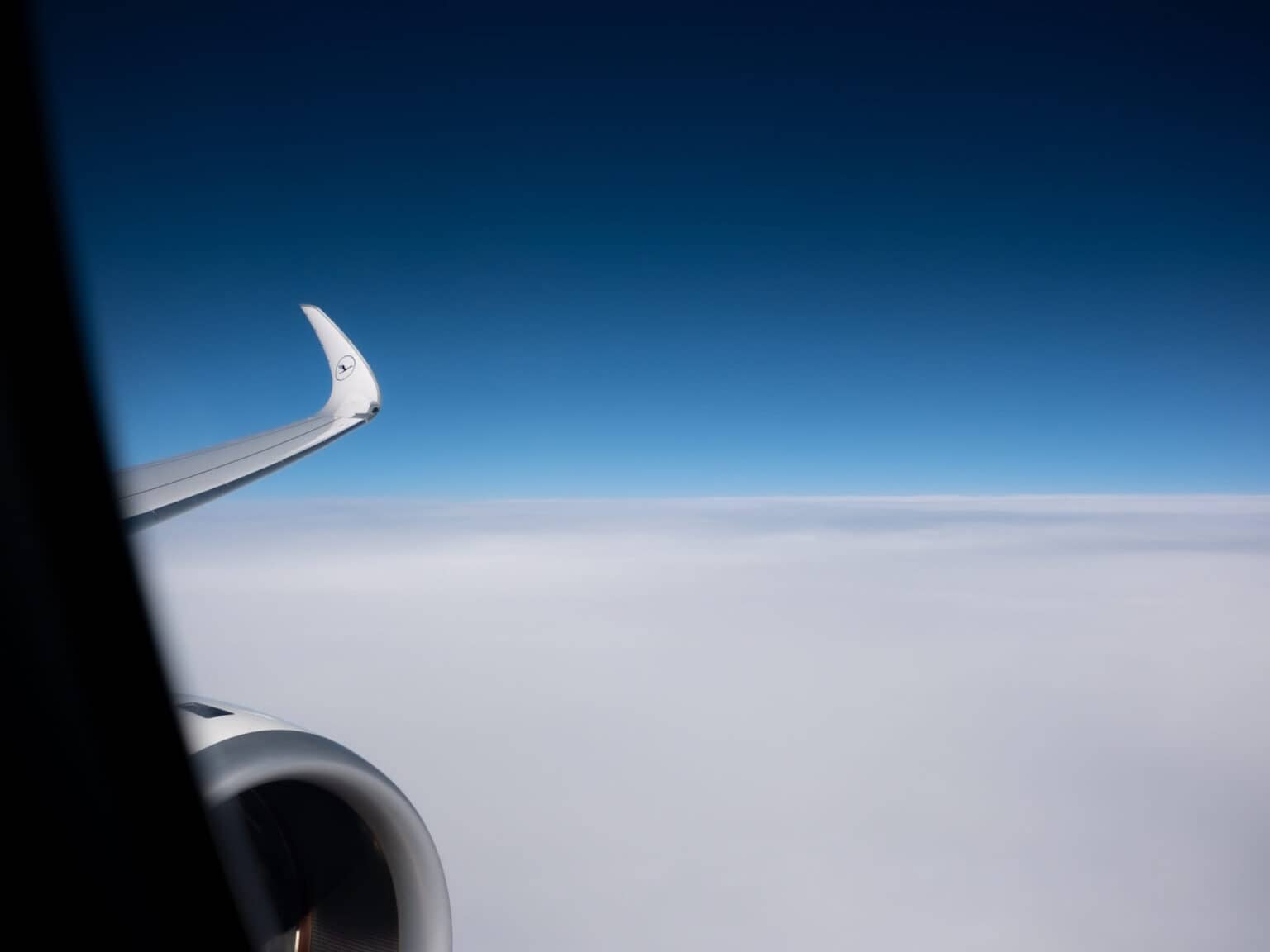 Ein Teil der Tragfläche und der Turbine eines Flugzeugs. Im Hintergrund eine weiße Wolkendecke, darüber der blaue Himmel.