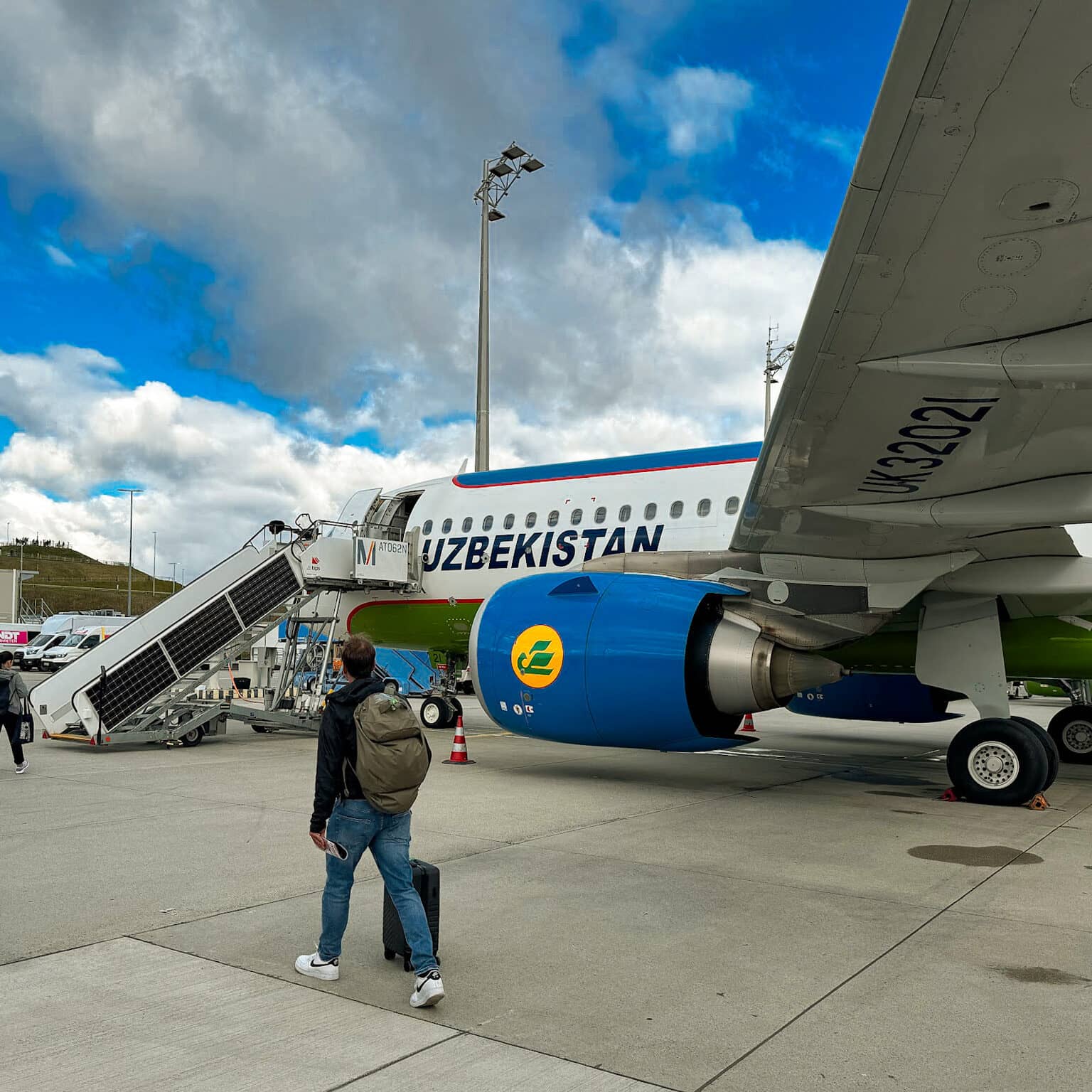 Ein Flugzeug der Fluggesellschaft Uzbekistan Airways auf dem Rollfeld. Mehrere Passagiere sind auf dem Weg zum Einstieg über eine Treppe.