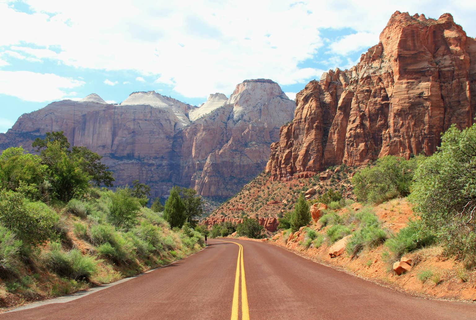Eine rotbraune Straße führt durch eine Schlucht, die von rotbraunen Felsen umgeben ist.