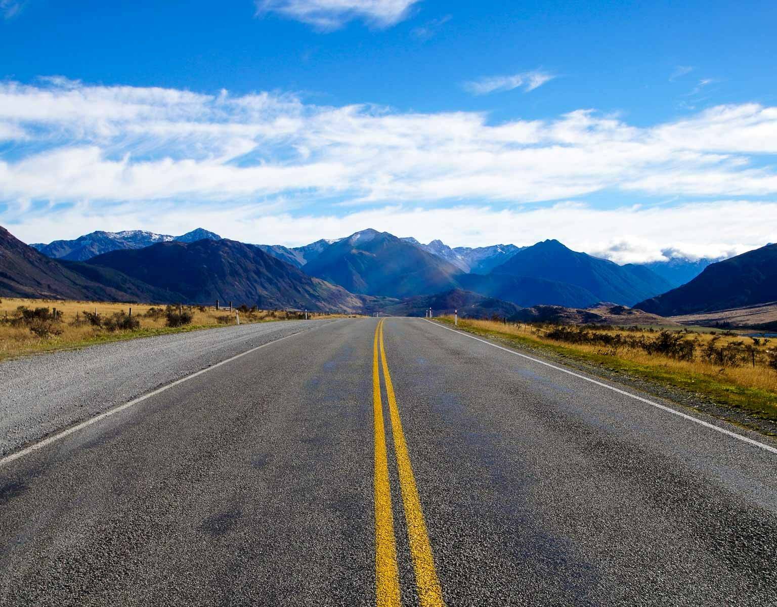 Eine leere Straße in Neuseeland führt geradeaus in das Bergpanorama.