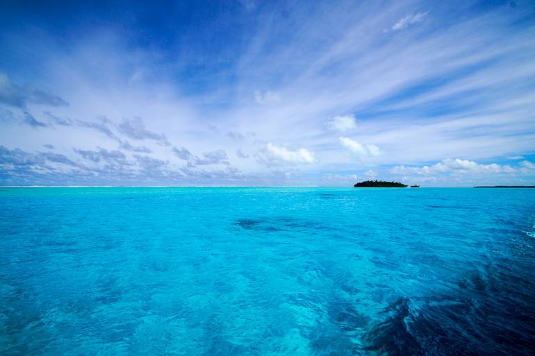 Eine kleine Insel liegt inmitten des glasklarem Meer der Cook Inseln bei Aitutaki, Ozeanien.