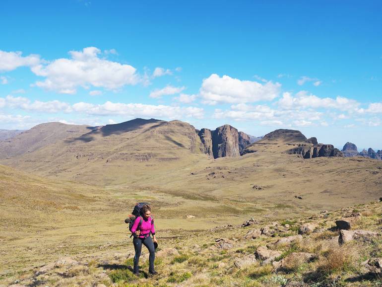 Südafrika Drakensberge: Eine Frau in einem Tal mit einem Rucksack auf dem Rücken.