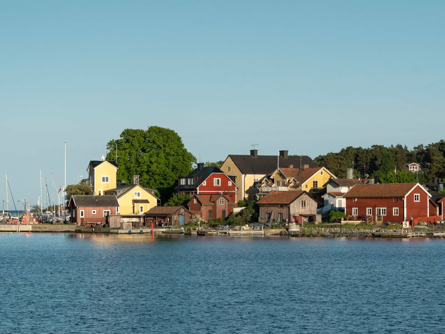 Ein kleines Dorf mit Holzhäusern in verschiedenen Farben und ein kleiner Hafen auf der Schäreninsel Sandhamn.