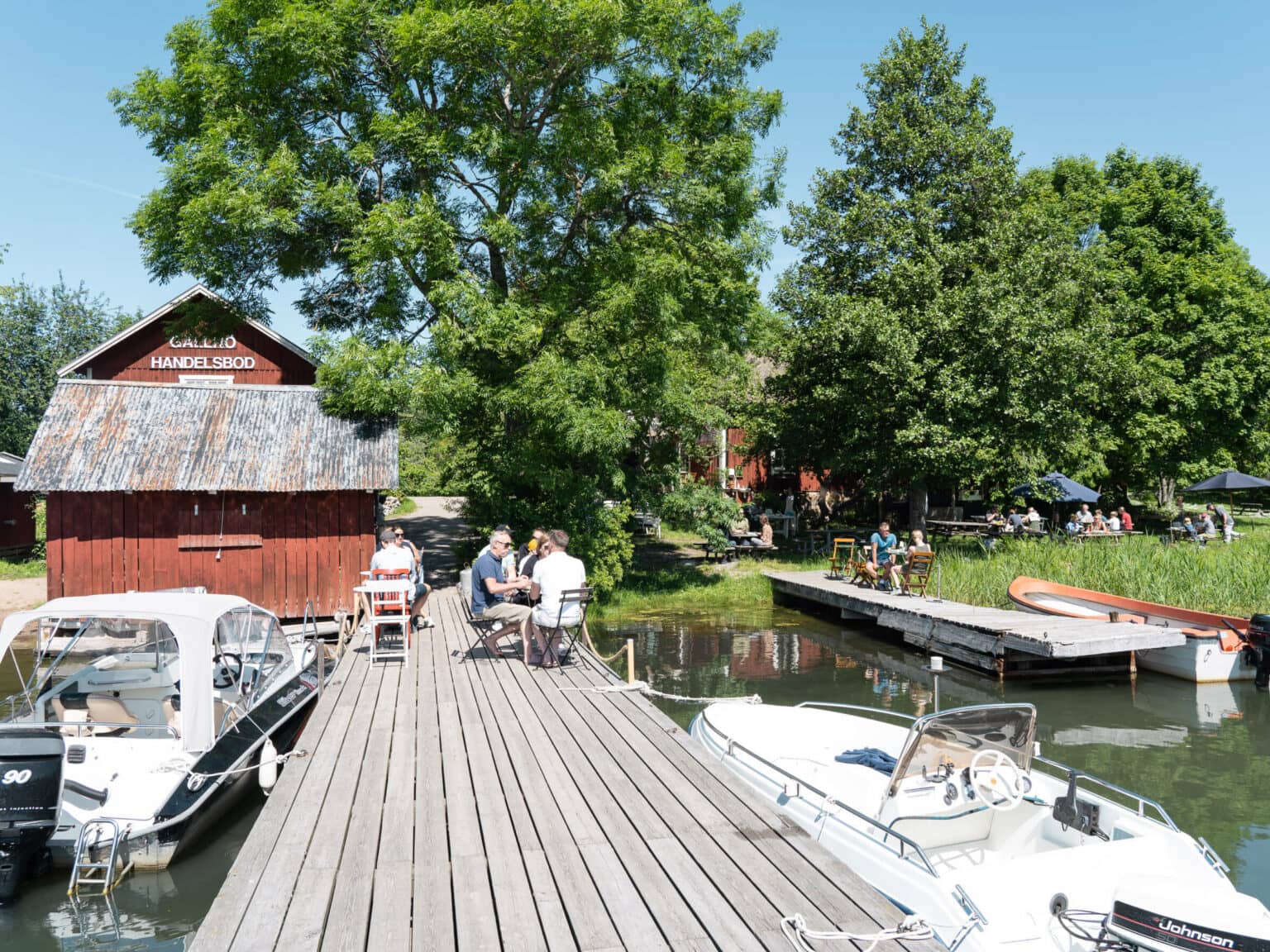 Direkt am hölzernen Anlegersteg zwischen den kleinen Motorbooten sitzen die Gäste der Gällnö Bar auf Stühlen in der Sonne.