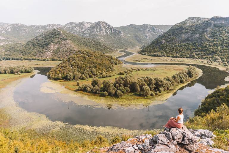 Eine Frau sitzt auf einem Stein und schaut auf die Flussschleife hinunter, die noch ein echter Geheimtipp in Montenegro ist.