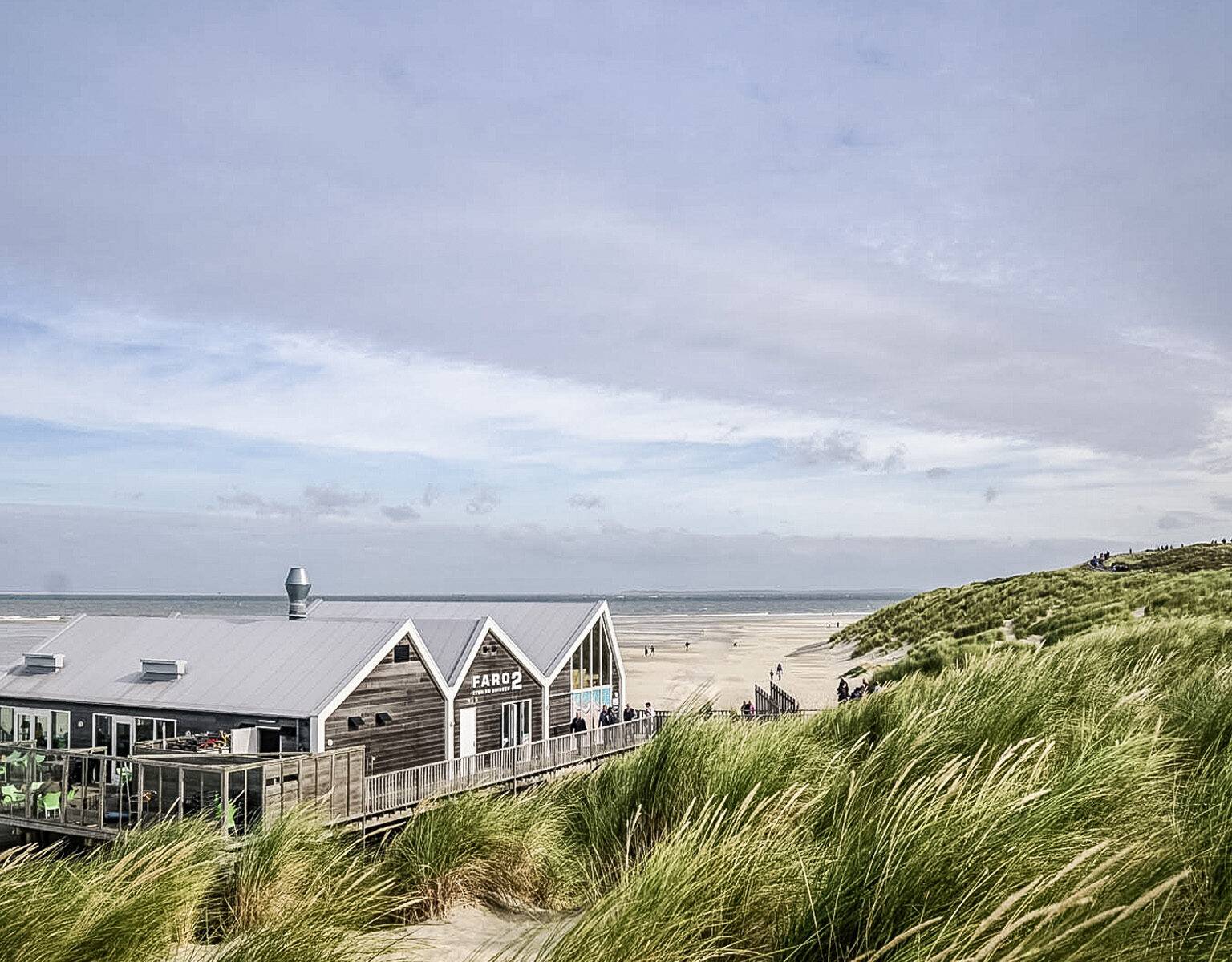 Blick auf Sandstrand und Meer in den Niederlanden, in der Ferne ein Leuchtturm und ein Fischerhaus
