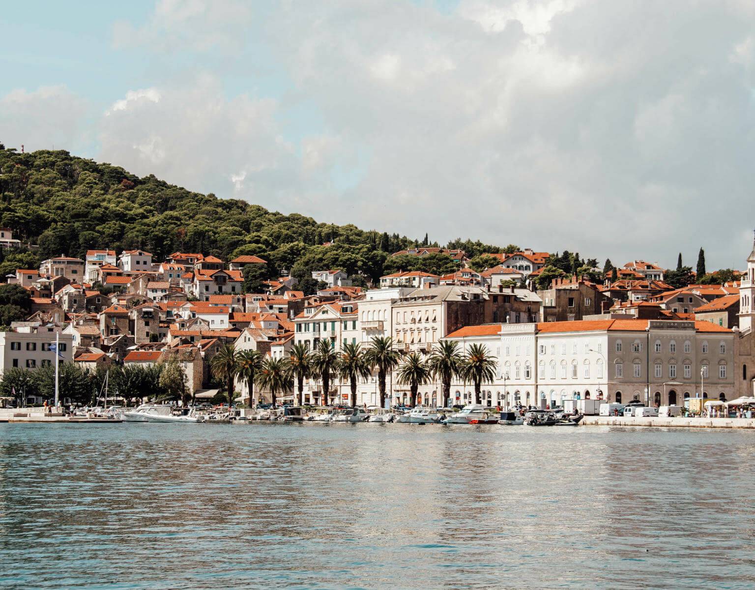Blick über das Meer auf die mit Palmen gesäumte Uferpromenade der Altstadt von Split.