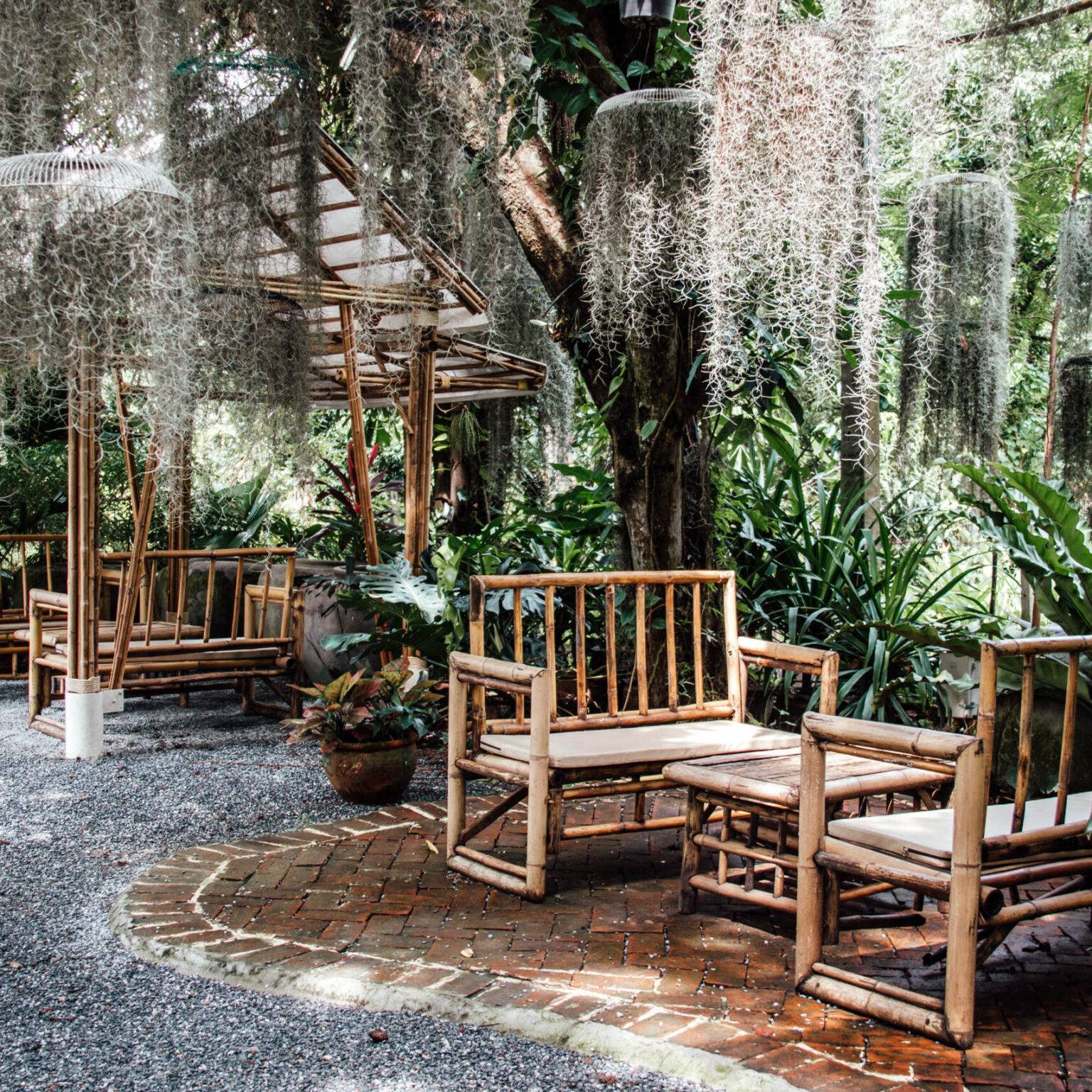 Bänke und Tische aus Bambus im Poomjai Garden umgeben von dschungelartigen Pflanzen.