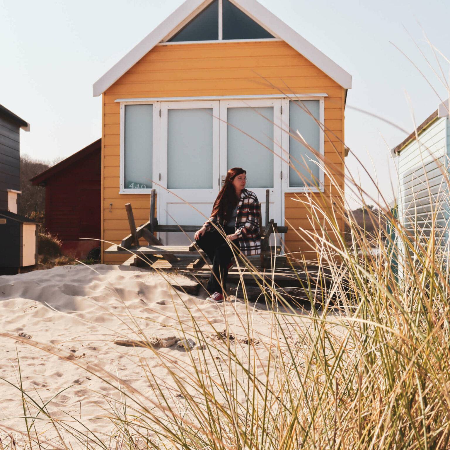 Eine Frau sitzt vor einer gelben Strandhütte im Mudeford Sands in Südengland.
