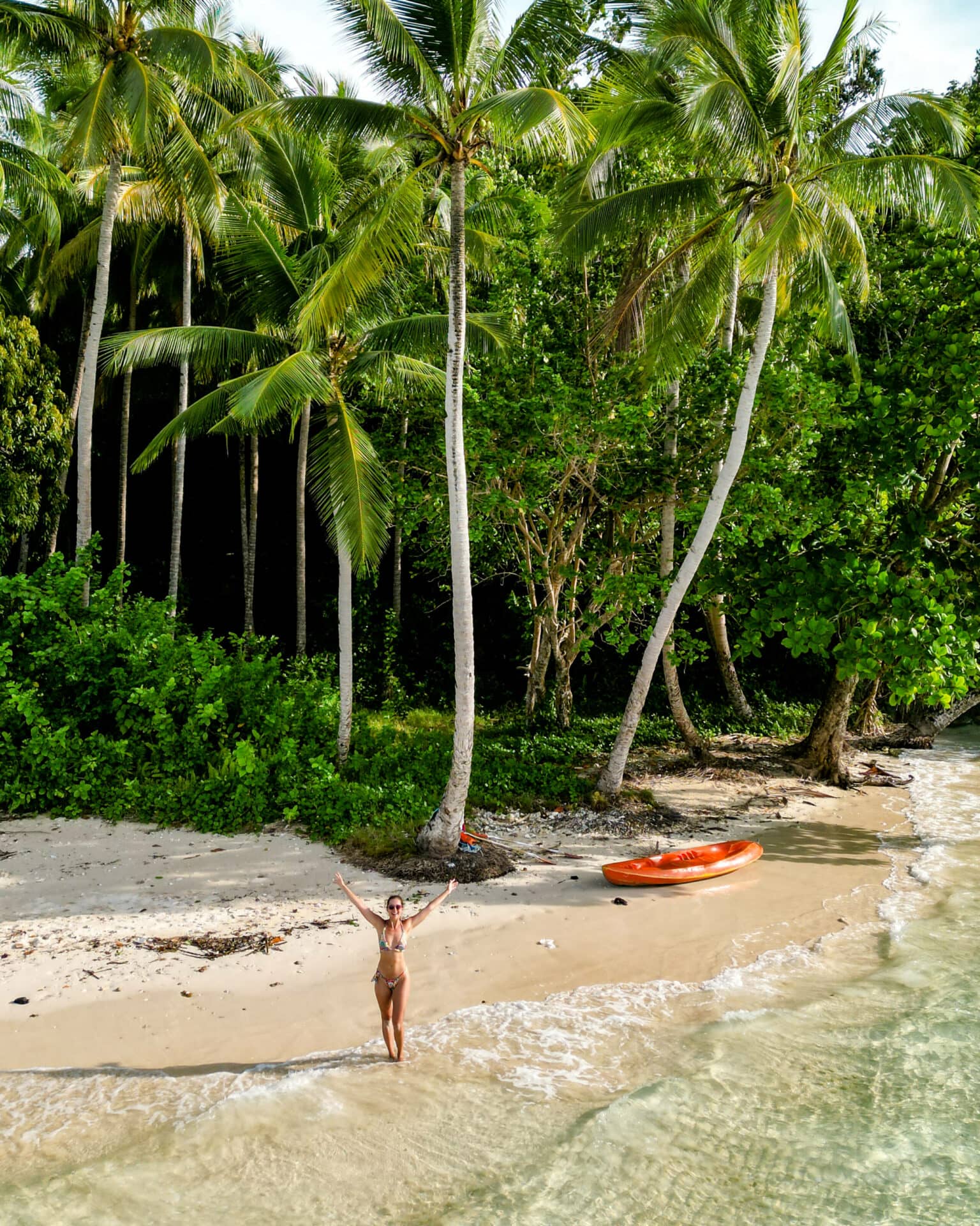 Bloggerin Nina steht an einem einsamen Strand auf Raja Ampat mit einem orangenen Kajak.