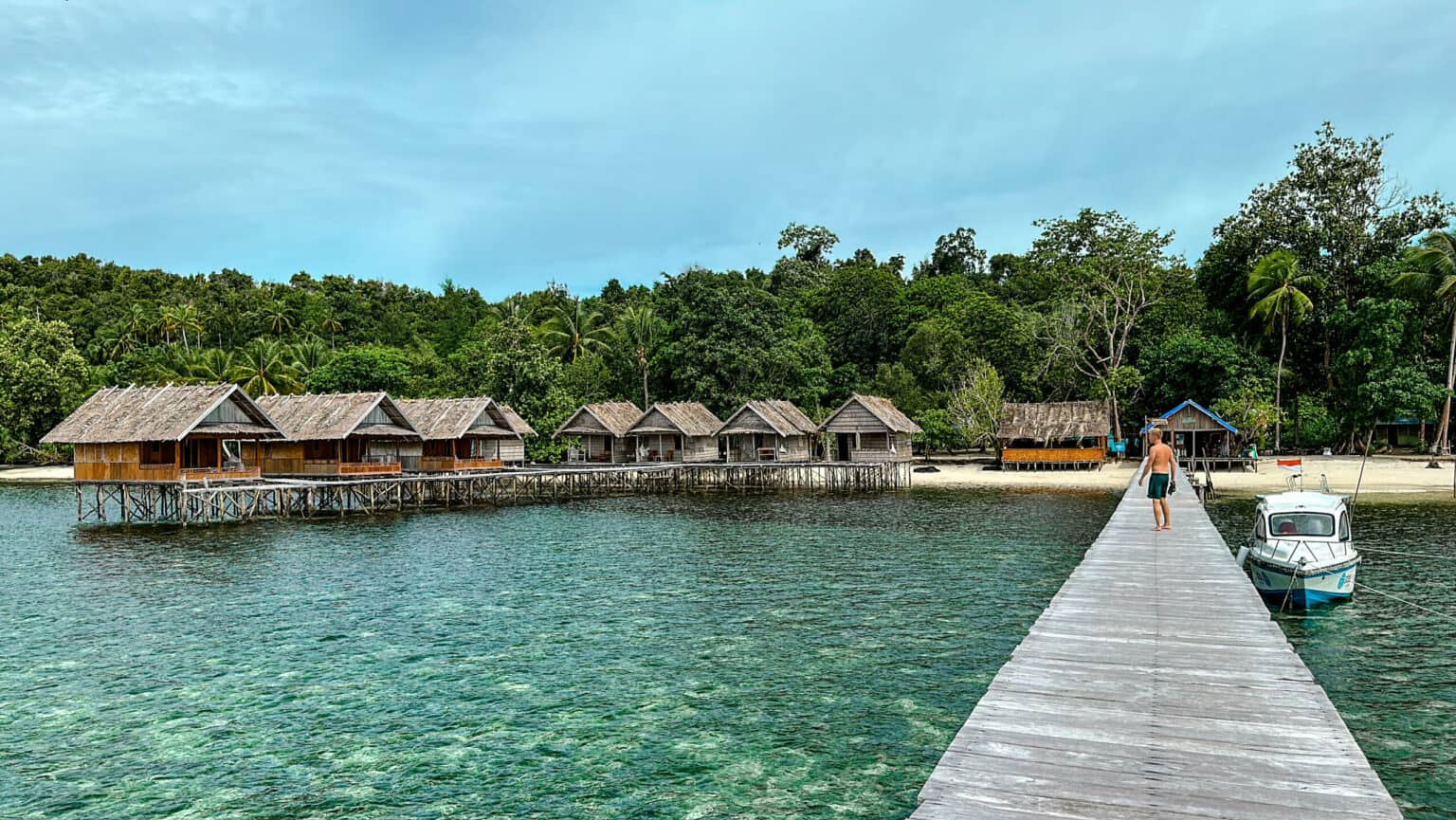 Blogger Tom steht auf einem Holzsteg und blickt auf die Over-Water-Bungalows eines Homestays auf Raja Ampat.