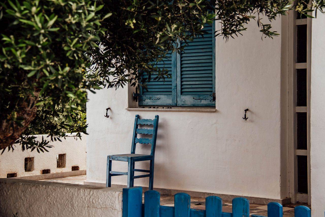 Vor einem weißen Haus mit blauen Fensterläden steht ein blauer Holzstuhl im Ort Koutsounari auf Kreta.