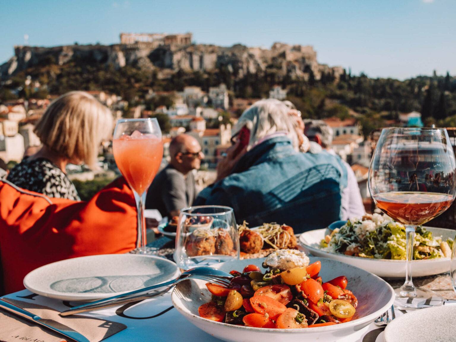 Speisen und Getränke stehen auf dem Tisch in der A for Athens Bar im Hintergrund sieht man die Akropolis.