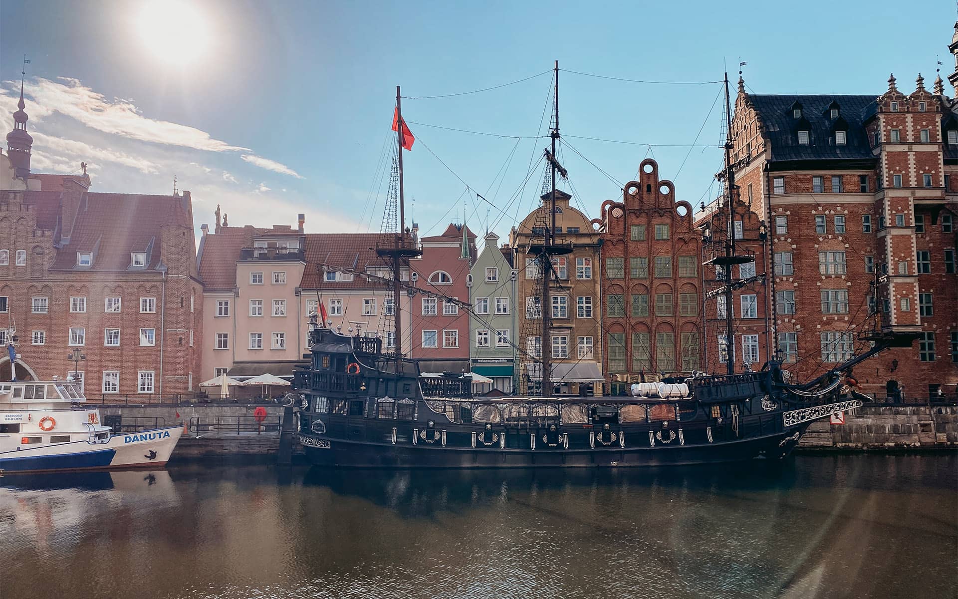 Ein altes Schiff steht im Wasser vor schönen, alten Reihenhäusern.
