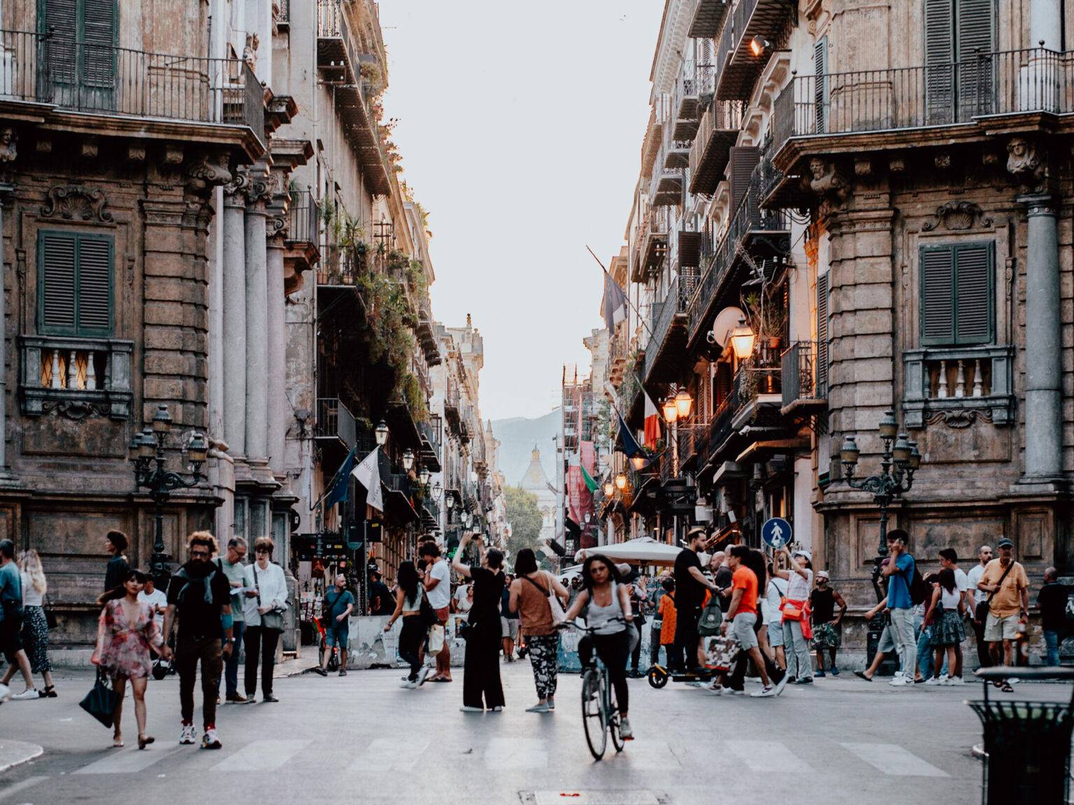 Eine wuselige Kreuzung in Mitten der Stadt Palermo, viele Menschen tummeln sich auf den Straßen.