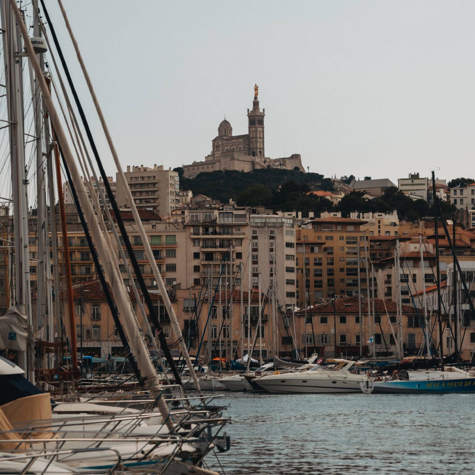 Der Hafen von Marseille mit vielen Segelbooten und im Hintergrund die bunten Häuser der Stadt.