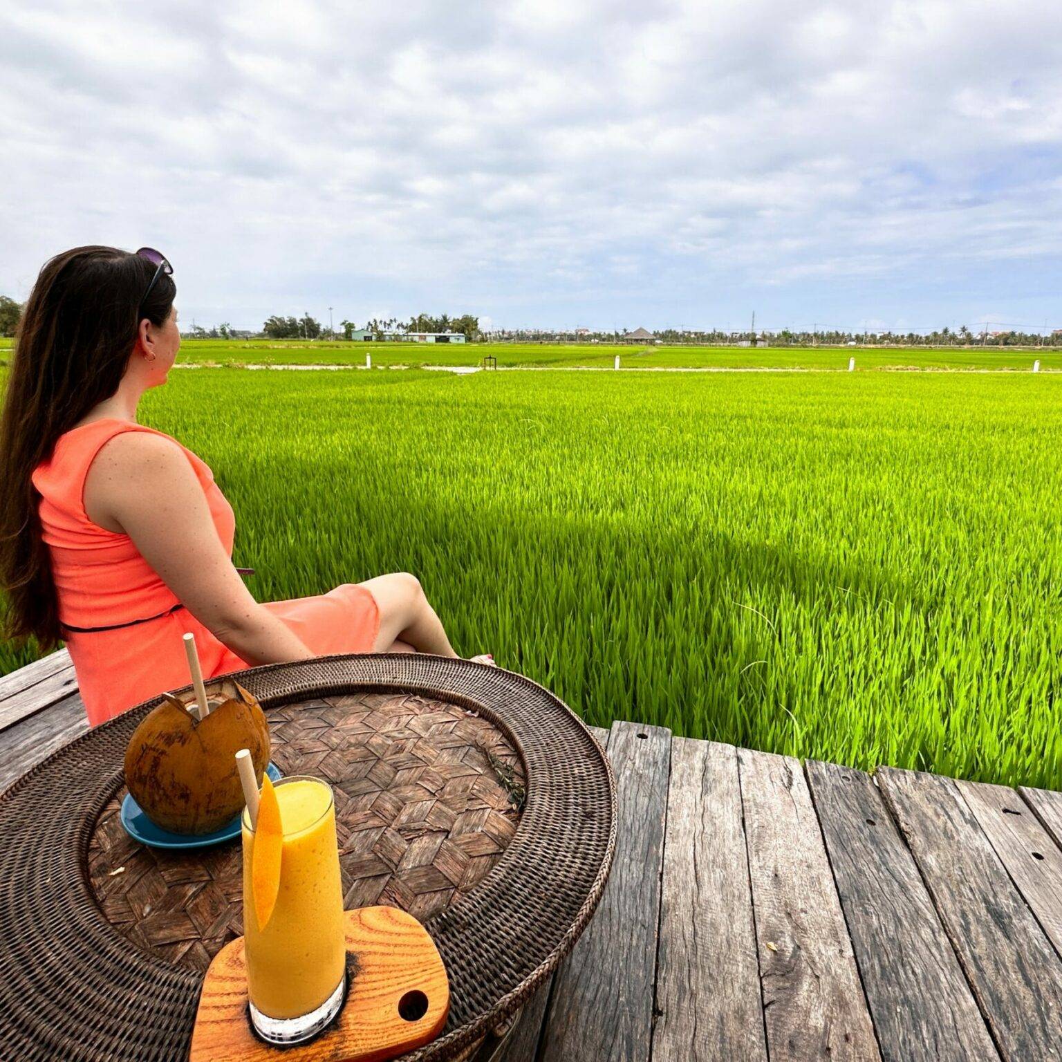 Biggi sitzt auf einer Plattform vor den grünen Reisfeldern.