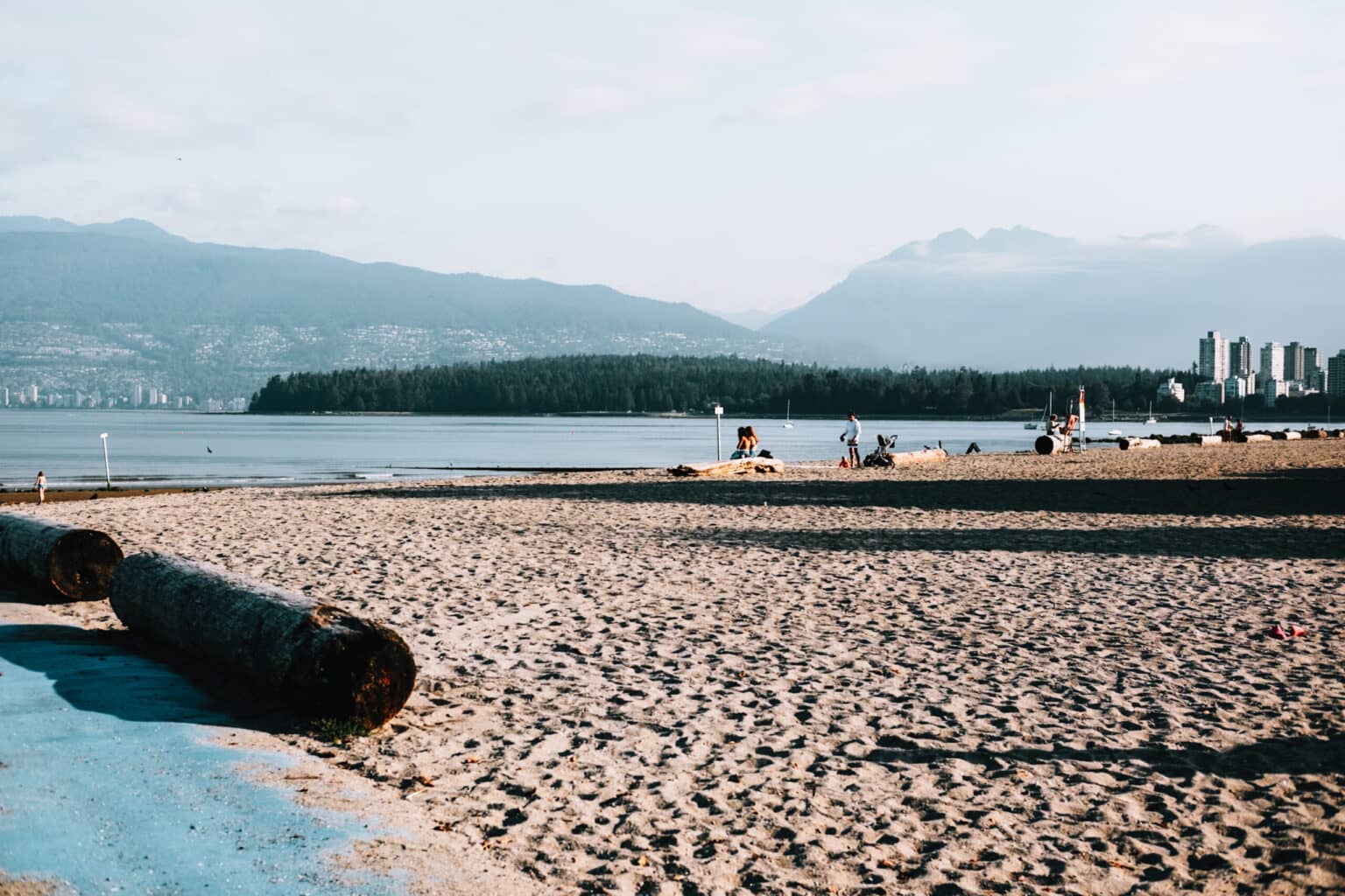 Vereinzelt sitzen Menschen auf Baumstämmen am Kitsilano Beach.