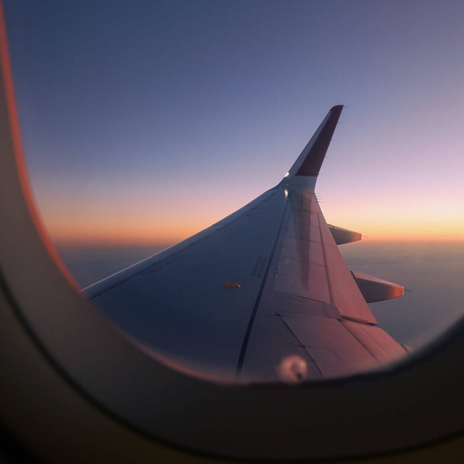 Ein Flugzeugträger hinter einem Flugzeugfenster. im Hintergrund geht die Sonne auf.