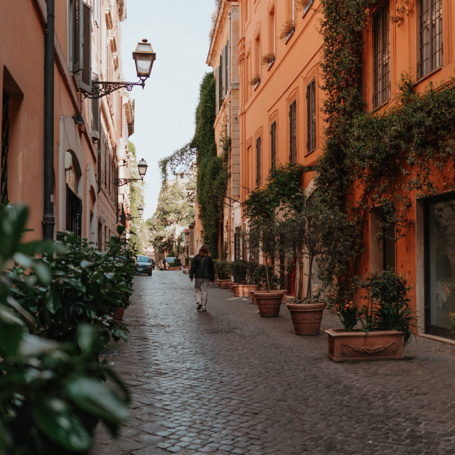 Eine junge Frau läuft die Via Margutta mit Kopfsteinpflaster und grün bewachsenen Häuserfassaden entlang.