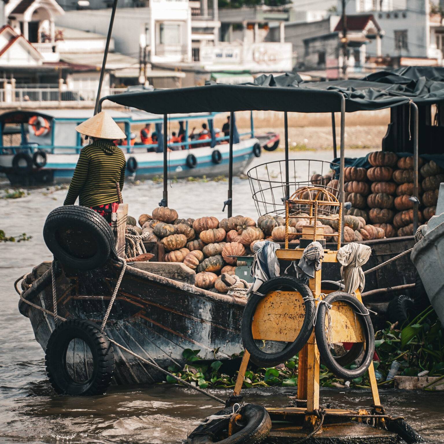 Auf einem mit Kürbissen vollgeladenen Boot sitzt ein Mann mit spitzem Strohhut.