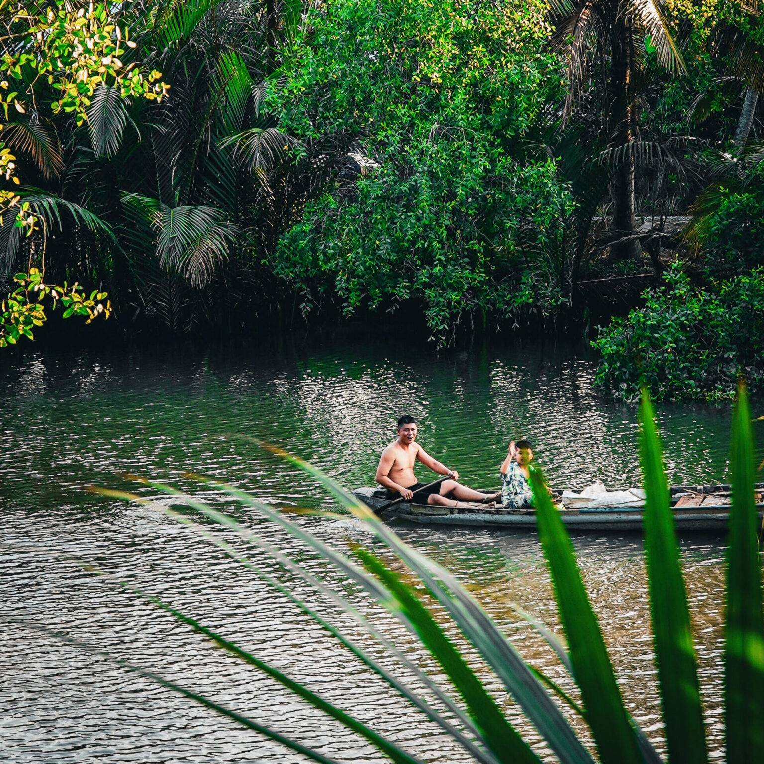 Vater und Sohn treiben auf einem langen Boot den von grünen Pflanzen umgebenen Fluss entlang.