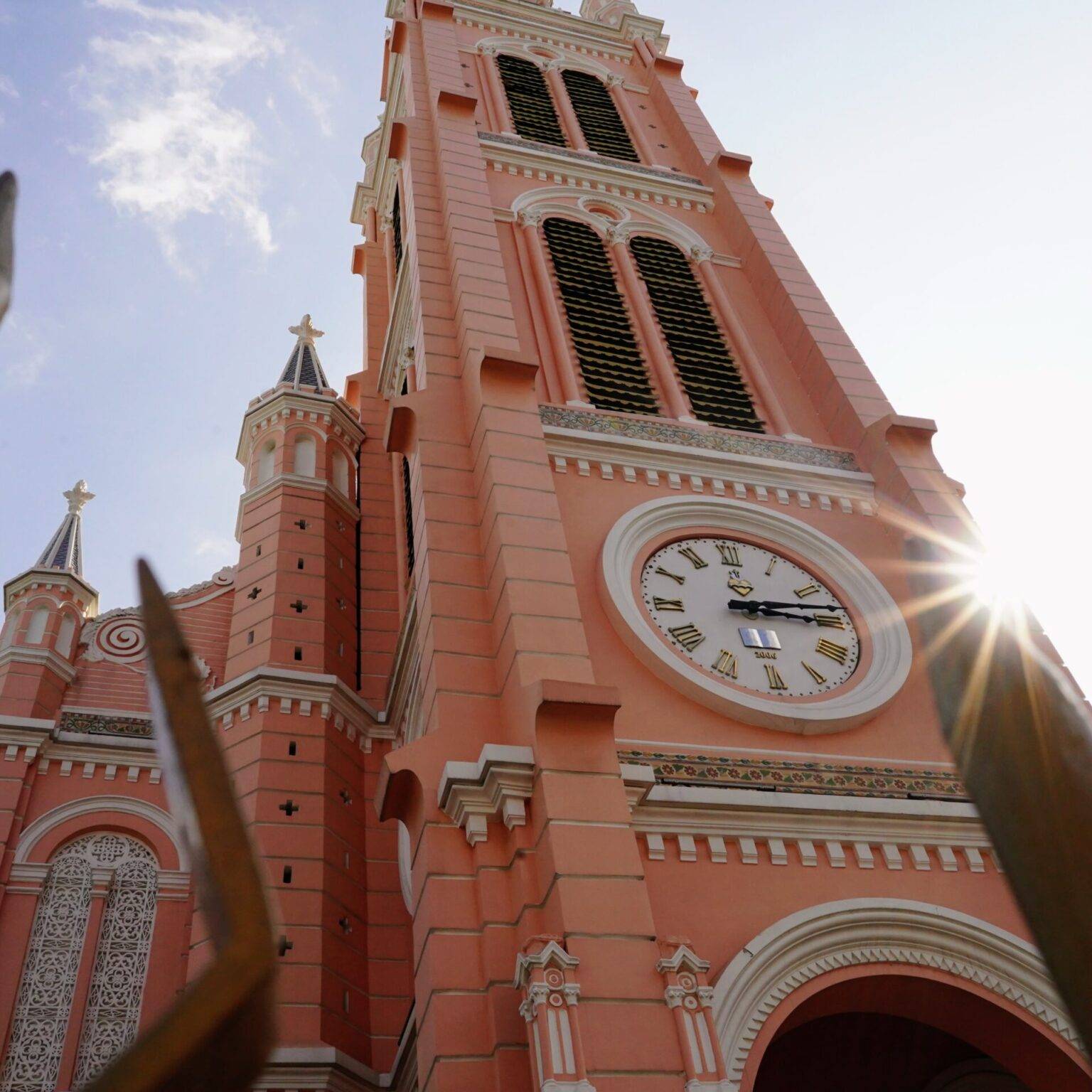 Die rosafarbene Fassade der Pink Church in Ho Chi Minh City mit einem zentralen hohen Turm und einer großen Uhr.