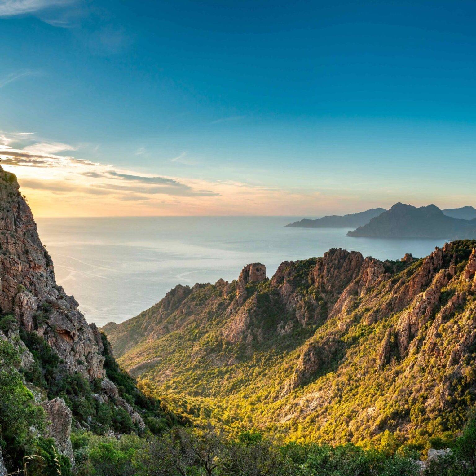 Die untergehende Sonne über dem Mittelmeer wirft ihr Licht auf die grün bewachsenen Hänge an der Ostküste Korsikas.